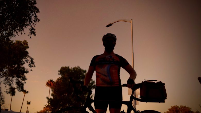 Bicyclist standing next to his bike against a dark ember sky