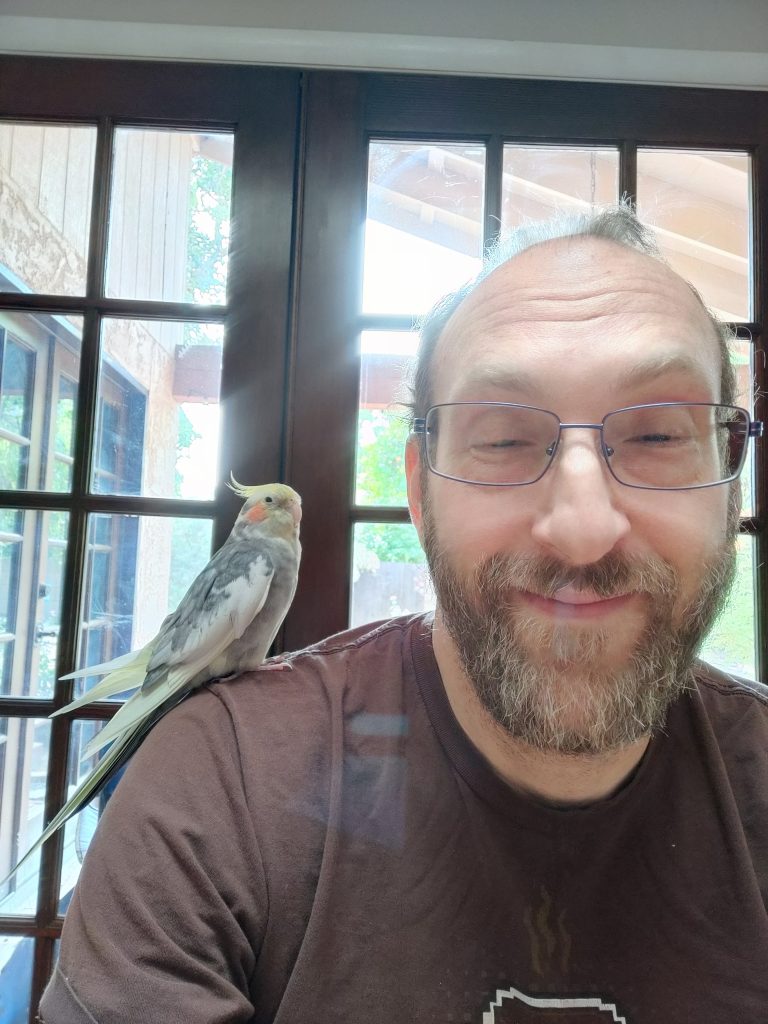 Harry sits in front of a window with a cockatiel on his shoulder