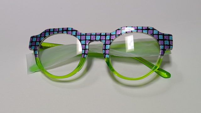 Green frames with a blue and shimmering lilac checker pattern across the brow